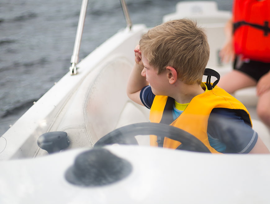 Young boy steering a boat wearing a yellow life jacket