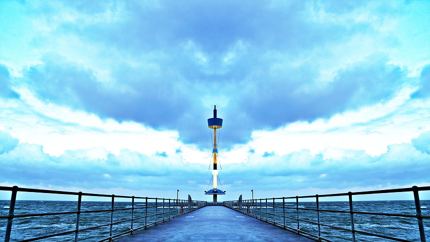 Blue pier leading to lighthouse under dramatic cloudy sky