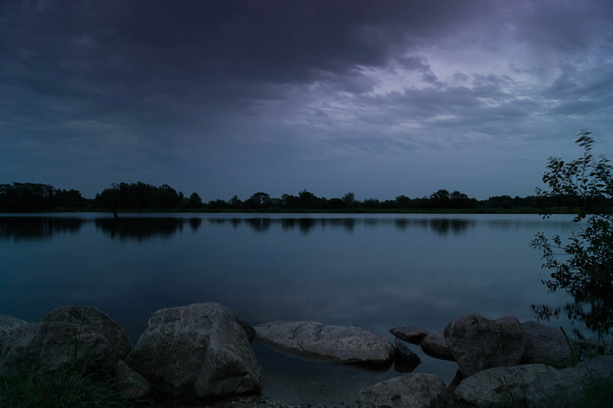 Dark moody lake landscape with rocks and trees at dusk