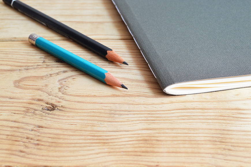 Gray notebook and pencils on wooden desk background
