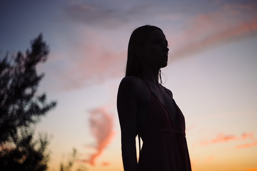Silhouette of a woman standing against a colorful sunset sky