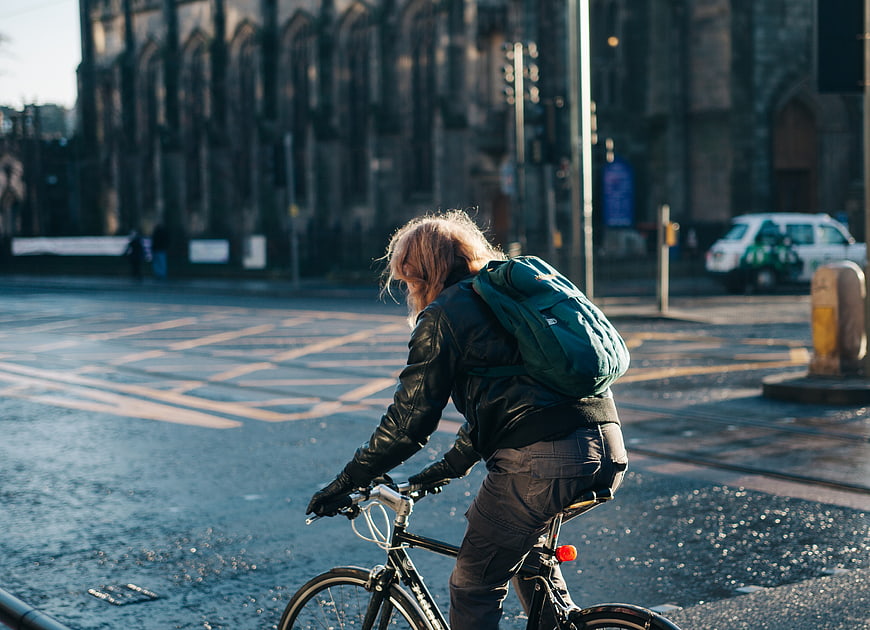Man cycling on wet city street with backpack