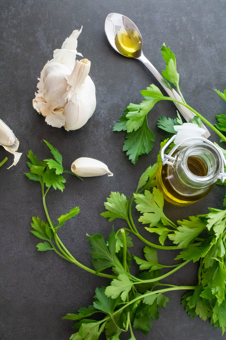 Fresh garlic, parsley, and olive oil on dark background
