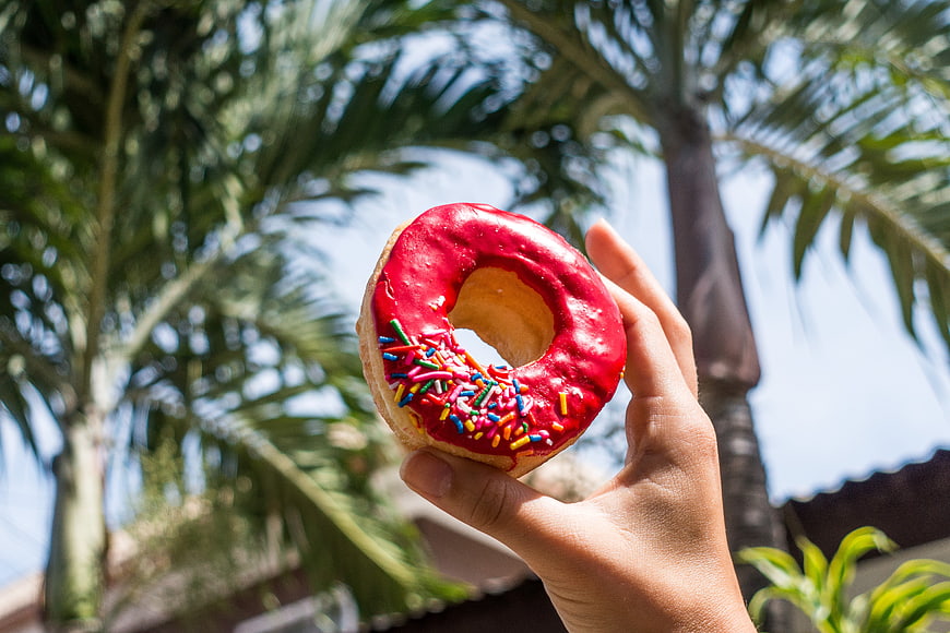 Hand Holding Red Glazed Donut with Sprinkles Outdoors