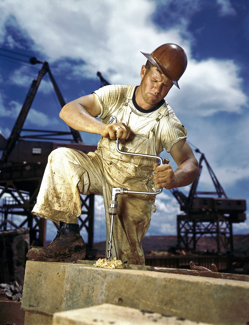 Hardworking construction worker drilling steel beam outdoors