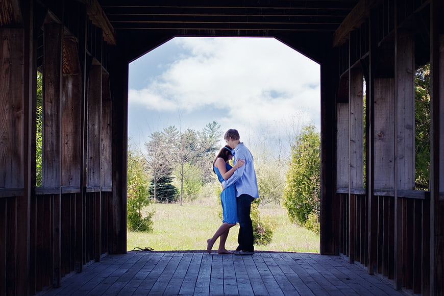 Couple embracing inside a rustic wooden covered bridge