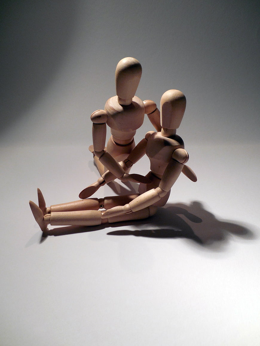 Two wooden artist mannequins sitting together on white background