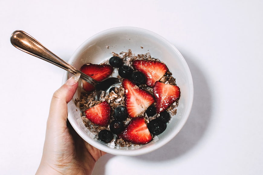 Overhead view of hand holding bowl of muesli with strawberries and blueberries
