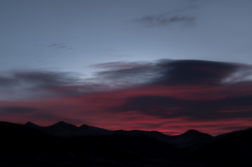 Dramatic red and purple sunset sky over dark mountain silhouette