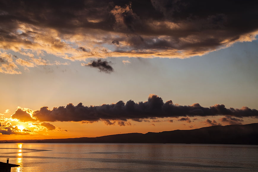 Dramatic sunset over calm sea with dark clouds and golden light