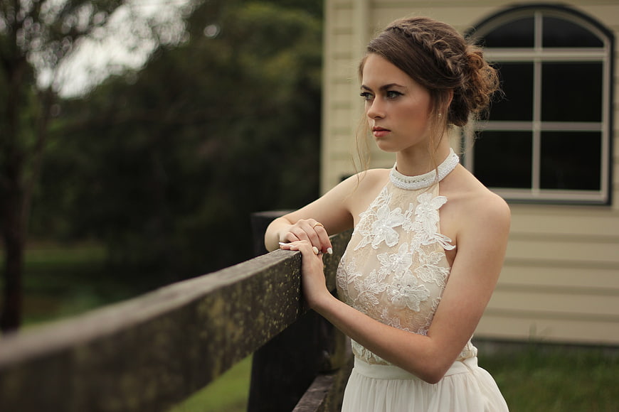 Pensive Woman in White Lace Dress Leaning on Wooden Railing