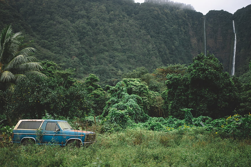 Vintage blue truck parked in lush tropical jungle with waterfall