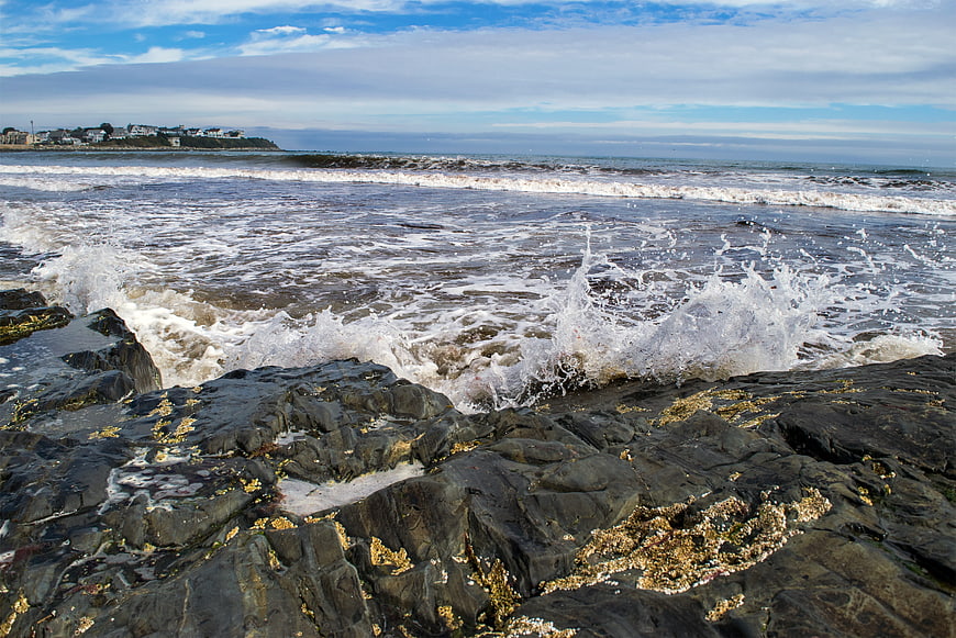 Ocean Waves Crashing on Rocky Shore with Coastal Houses