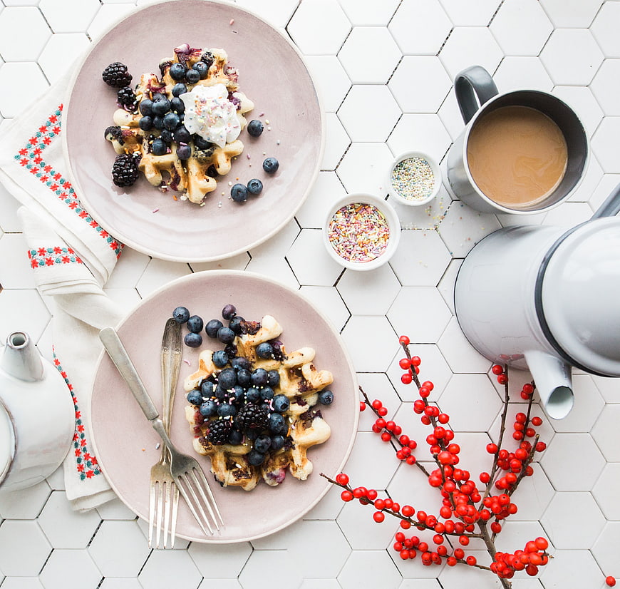 Overhead view of waffles with berries and coffee on white tiles
