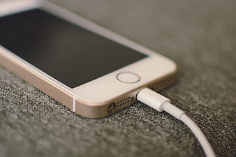 Close-up of white smartphone charging on textured surface
