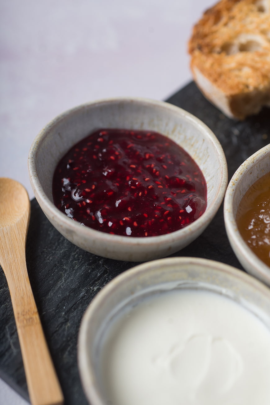Ceramic bowls of red currant jam, honey, and cream on slate