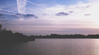 Serene Lake Sunset with Contrails and Silhouetted Trees