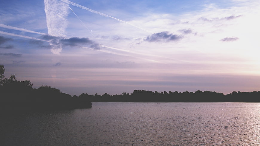 Serene Lake Sunset with Contrails and Silhouetted Trees