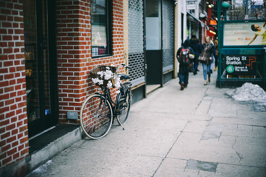 Bicycle with white flowers parked on city sidewalk near subway station
