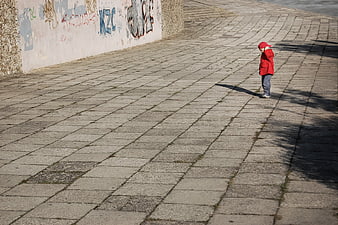 Lonely child in red jacket standing on paved urban square