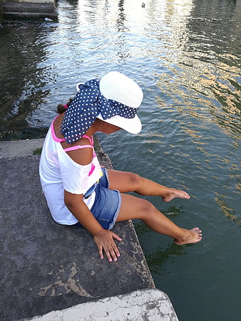 Young Girl Dipping Feet in Water by Riverbank