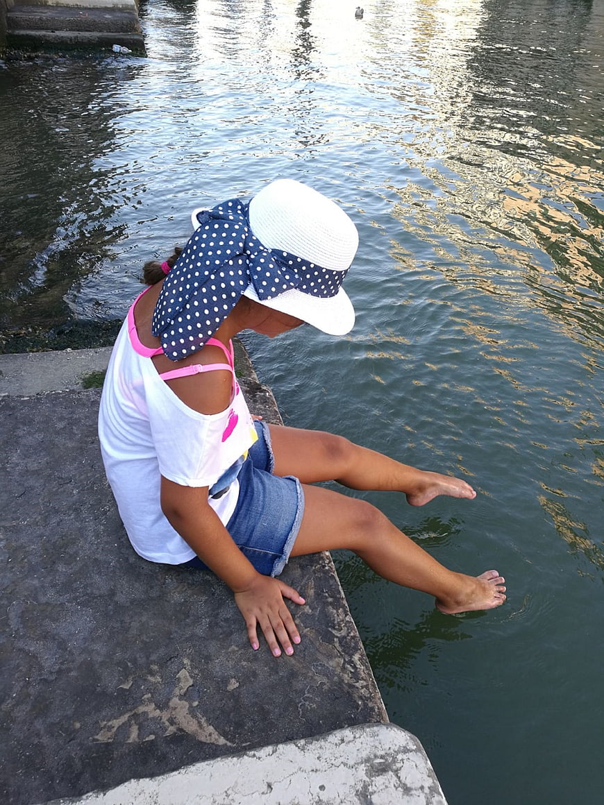 Young Girl Dipping Feet in Water by Riverbank