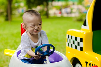 Happy toddler boy driving colorful ride-on toy car in park