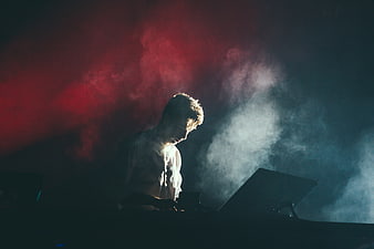 DJ performing on stage with dramatic red and blue smoke lighting