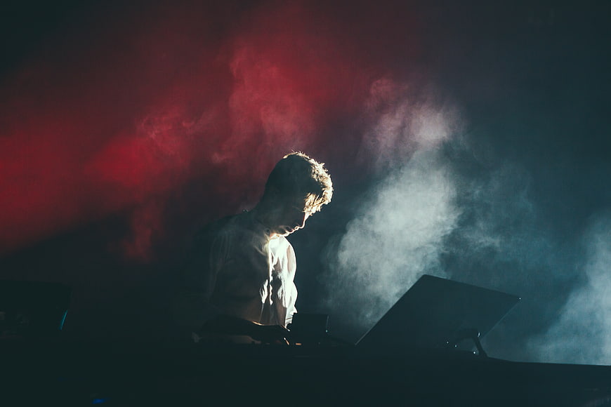 DJ performing on stage with dramatic red and blue smoke lighting