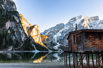 Rustic wooden cabin on stilts by alpine lake with snowy mountains