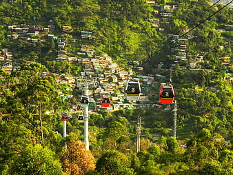 Metrocable gondolas traversing a lush green hillside with scattered housing in Colombia