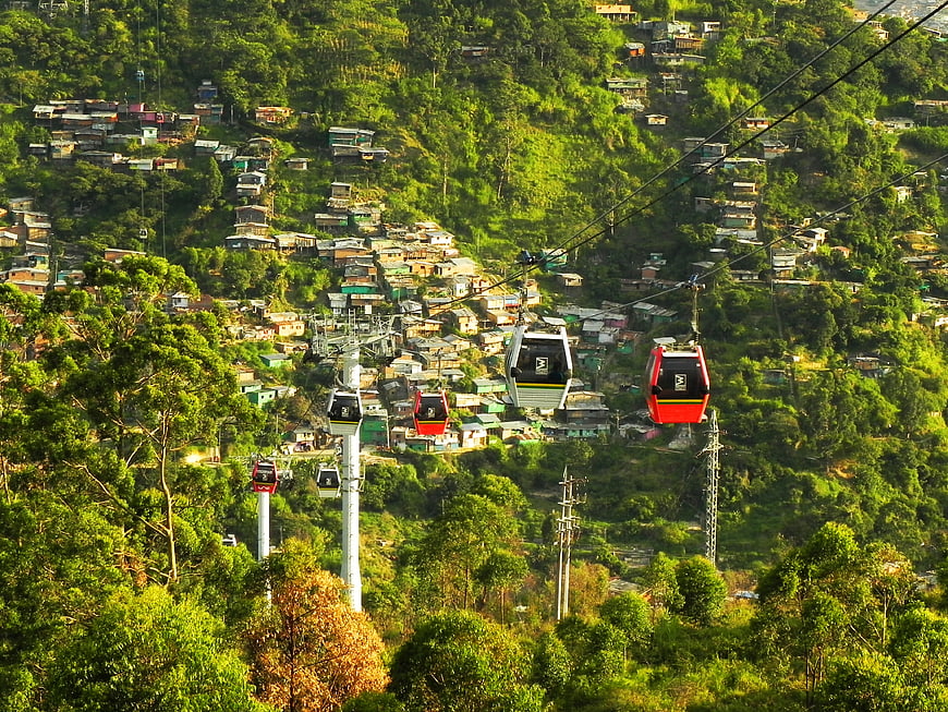 Metrocable gondolas traversing a lush green hillside with scattered housing in Colombia