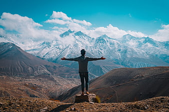 Man with open arms standing on mountain peak overlooking snowy range