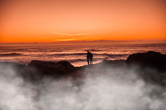 Silhouette of couple watching sunset over ocean waves