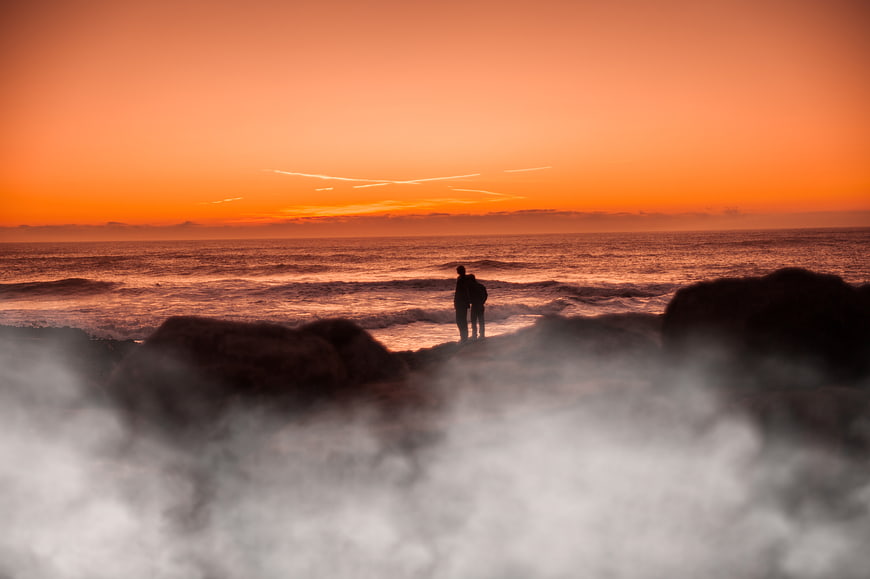 Silhouette of couple watching sunset over ocean waves