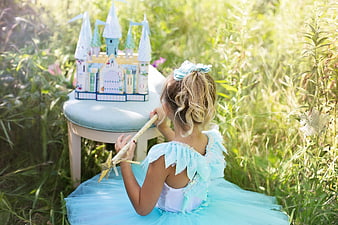 Little girl in blue princess dress playing with toy castle in field