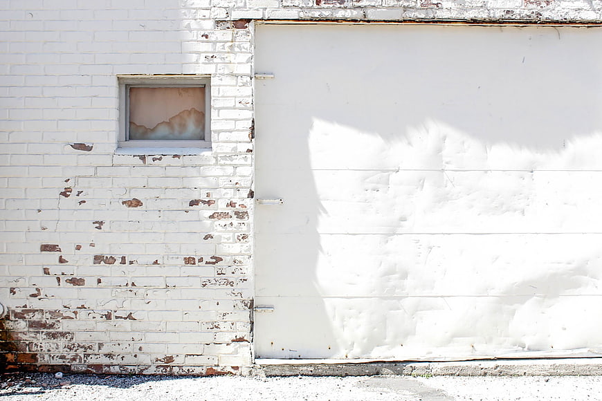 White brick wall with peeling paint and large garage door