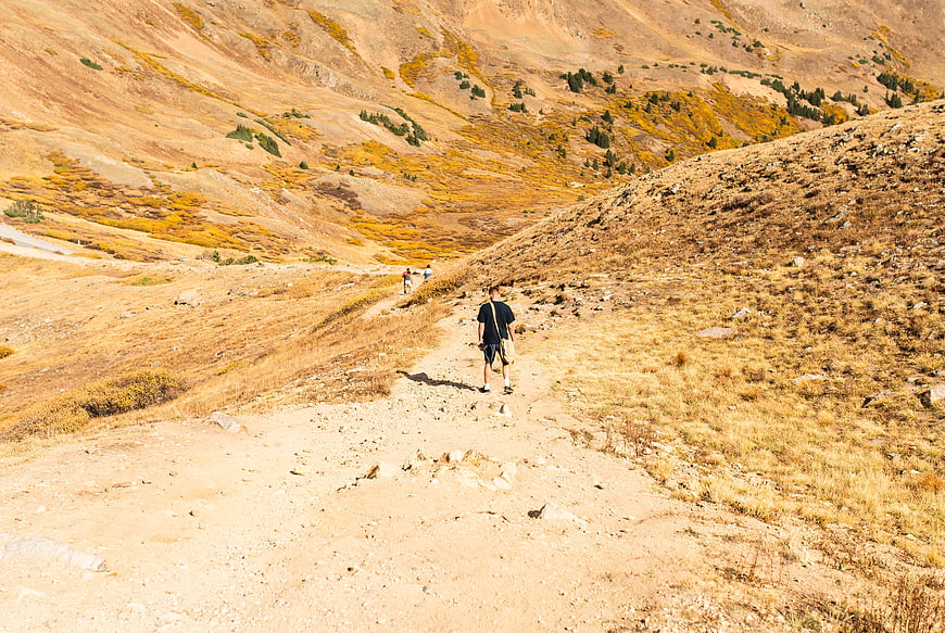 Hiker walking on dry mountain trail in autumn