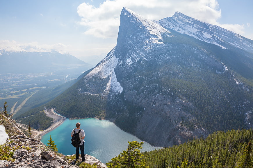 Hiker overlooking turquoise mountain lake and snowy peaks