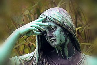 Close-up of weathered bronze statue of grieving woman in cemetery