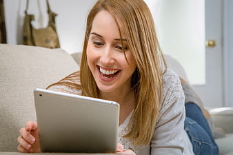 Happy woman laughing while using tablet on couch