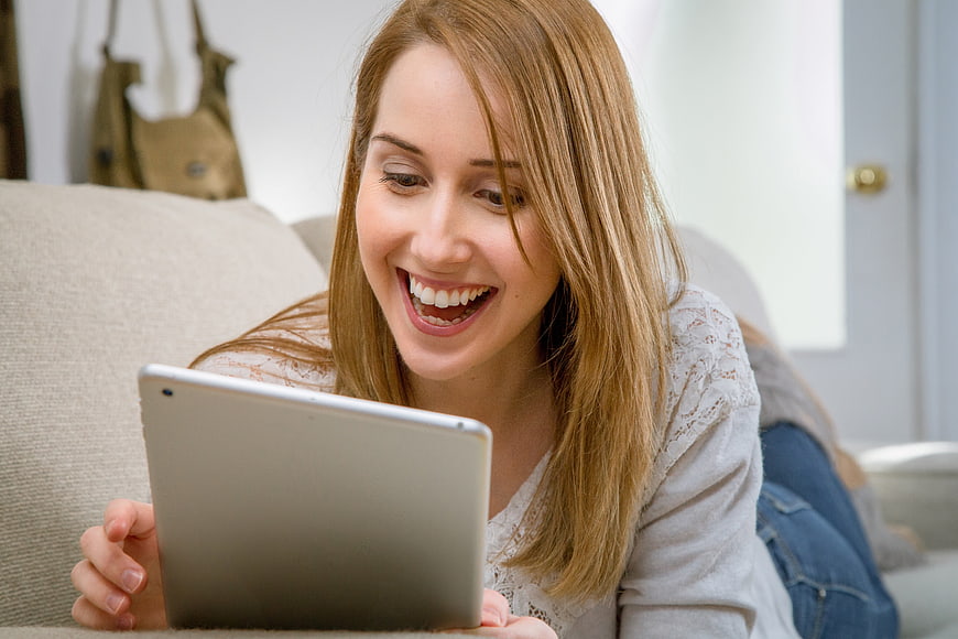 Happy woman laughing while using tablet on couch