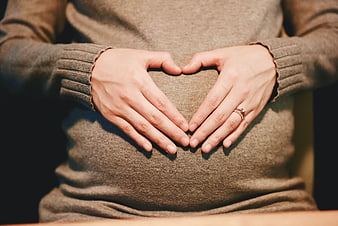 Pregnant woman making heart shape with hands on belly