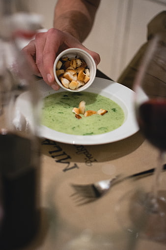 Hand adding croutons to green spinach soup in restaurant