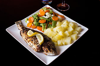 Grilled whole fish with potatoes and mixed vegetables on white plate