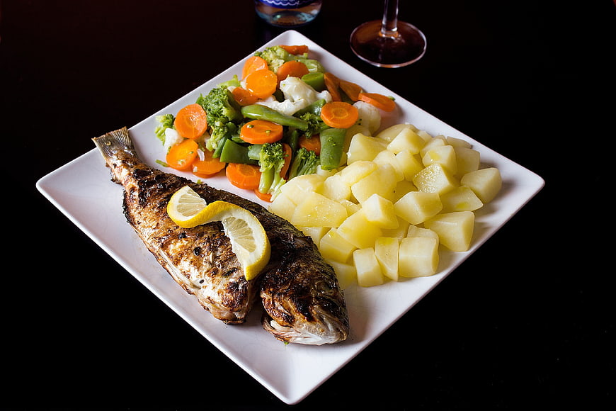 Grilled whole fish with potatoes and mixed vegetables on white plate