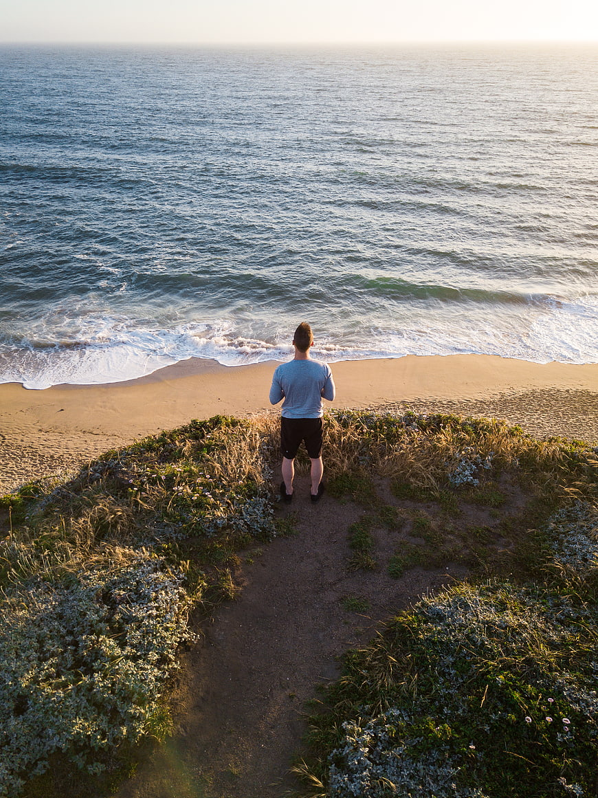 Man standing on cliff overlooking ocean at sunset