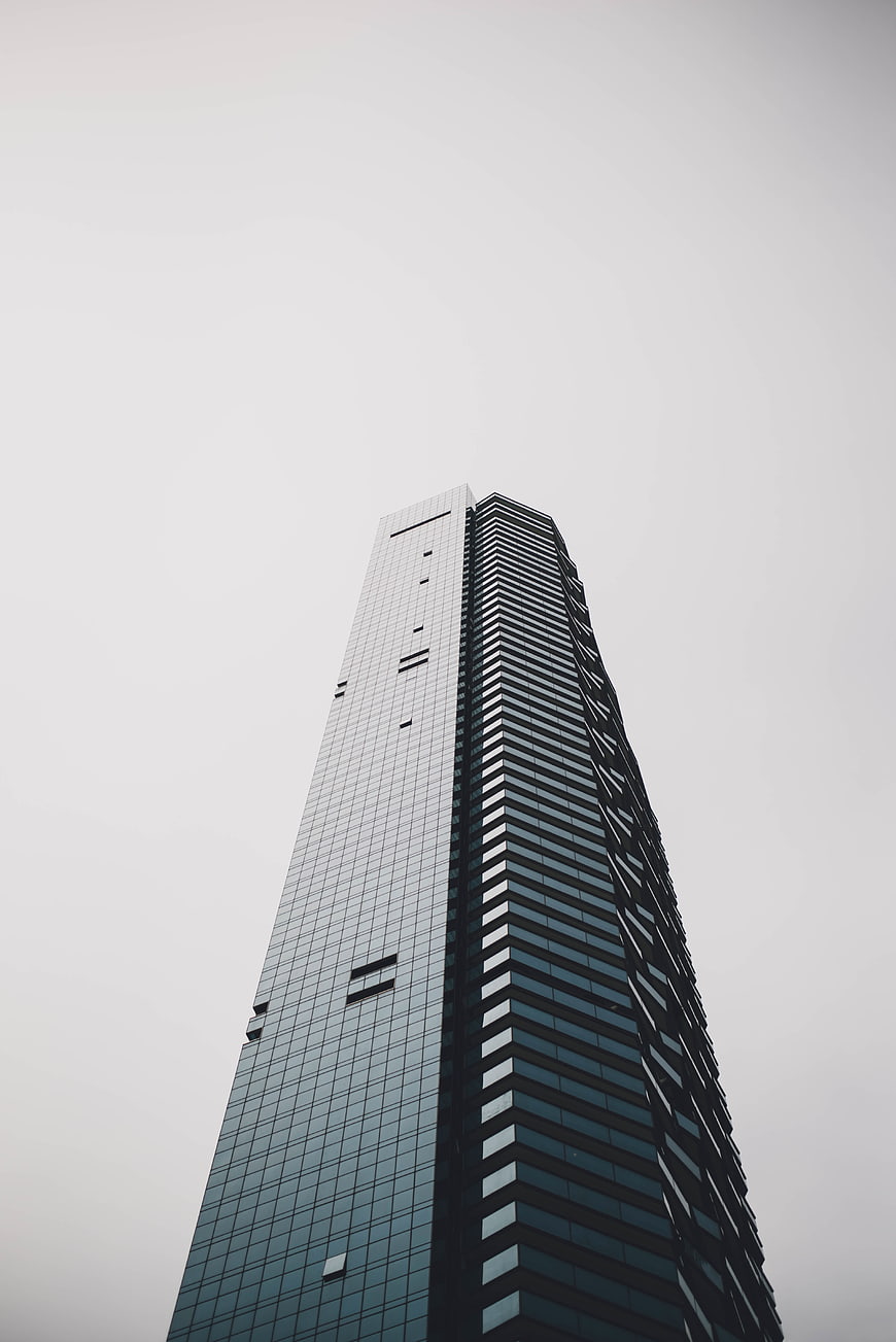 Low angle view of modern glass skyscraper against gray sky