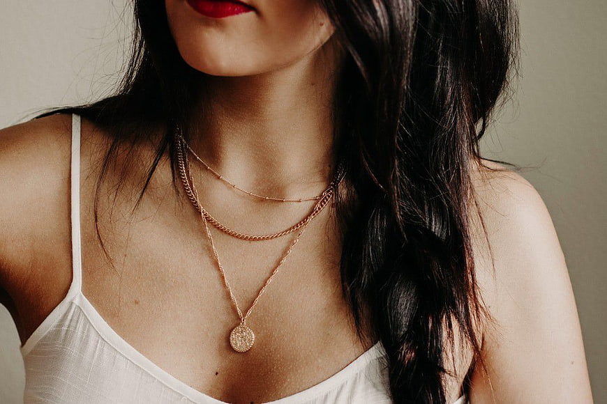 Close-up of woman wearing layered gold necklaces and white tank top