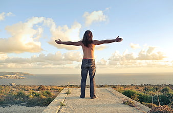 Man with arms outstretched overlooking ocean sunset